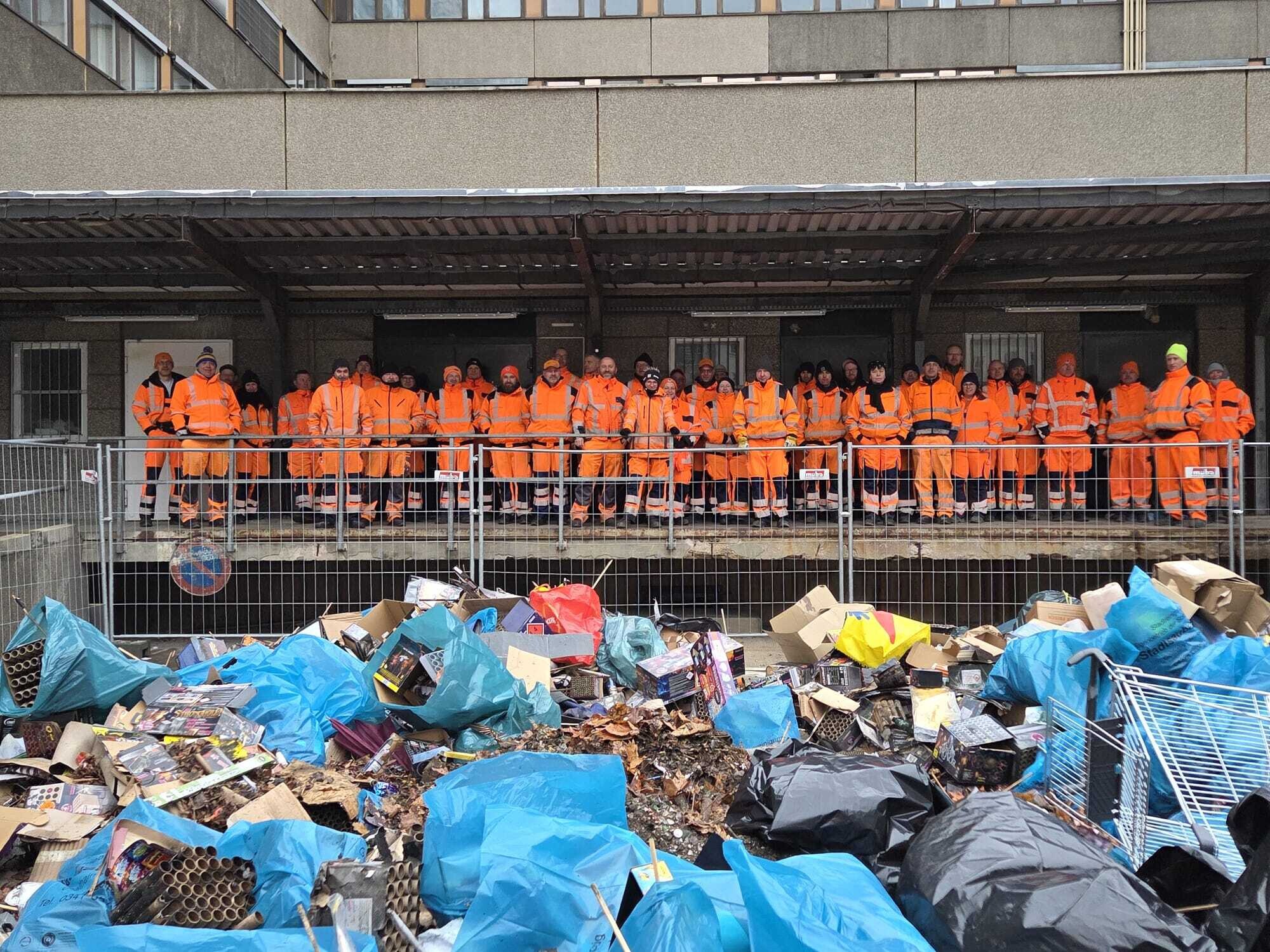 Mitarbeitende der Stadtreinigung stehen vor einem gro&szlig;en Haufen Silvesterabfall.
