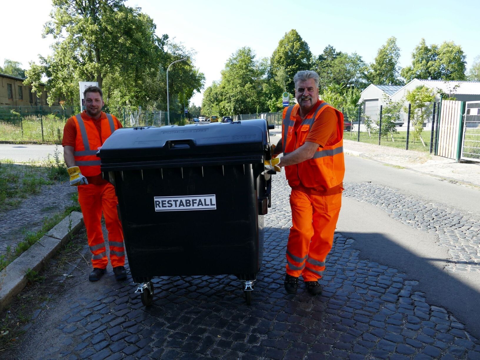 Zwei Müllarbeiter schieben gemeinsam eine Restabfalltonne