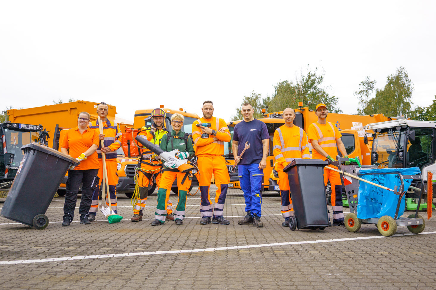 8 Mitarbeiterinnen und Mitarbeiter in Arbeitskleidung aus verschiedenen Bereichen der Stadtreinigung mit passenden Utensilien