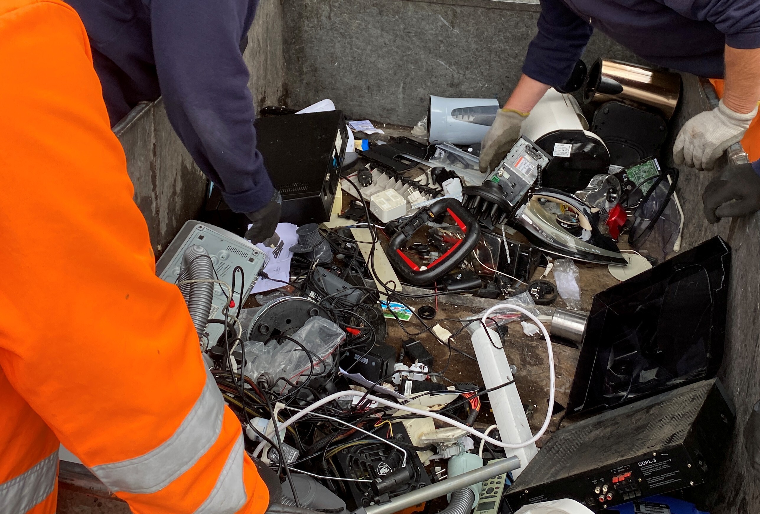 Blick in einen Container mit Elektroschrott. H&auml;nde sortieren verschiedene Ger&auml;te