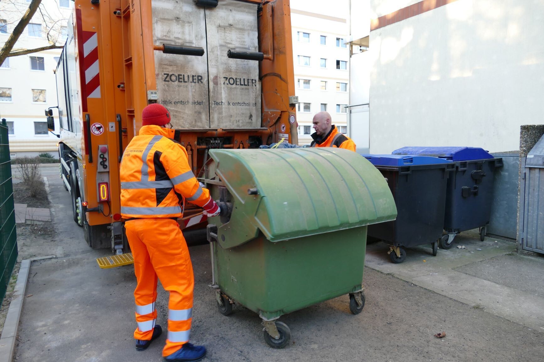 Zwei M&uuml;llwerker schieben eine Tonne zum Abfallsammelfahrzeug.
