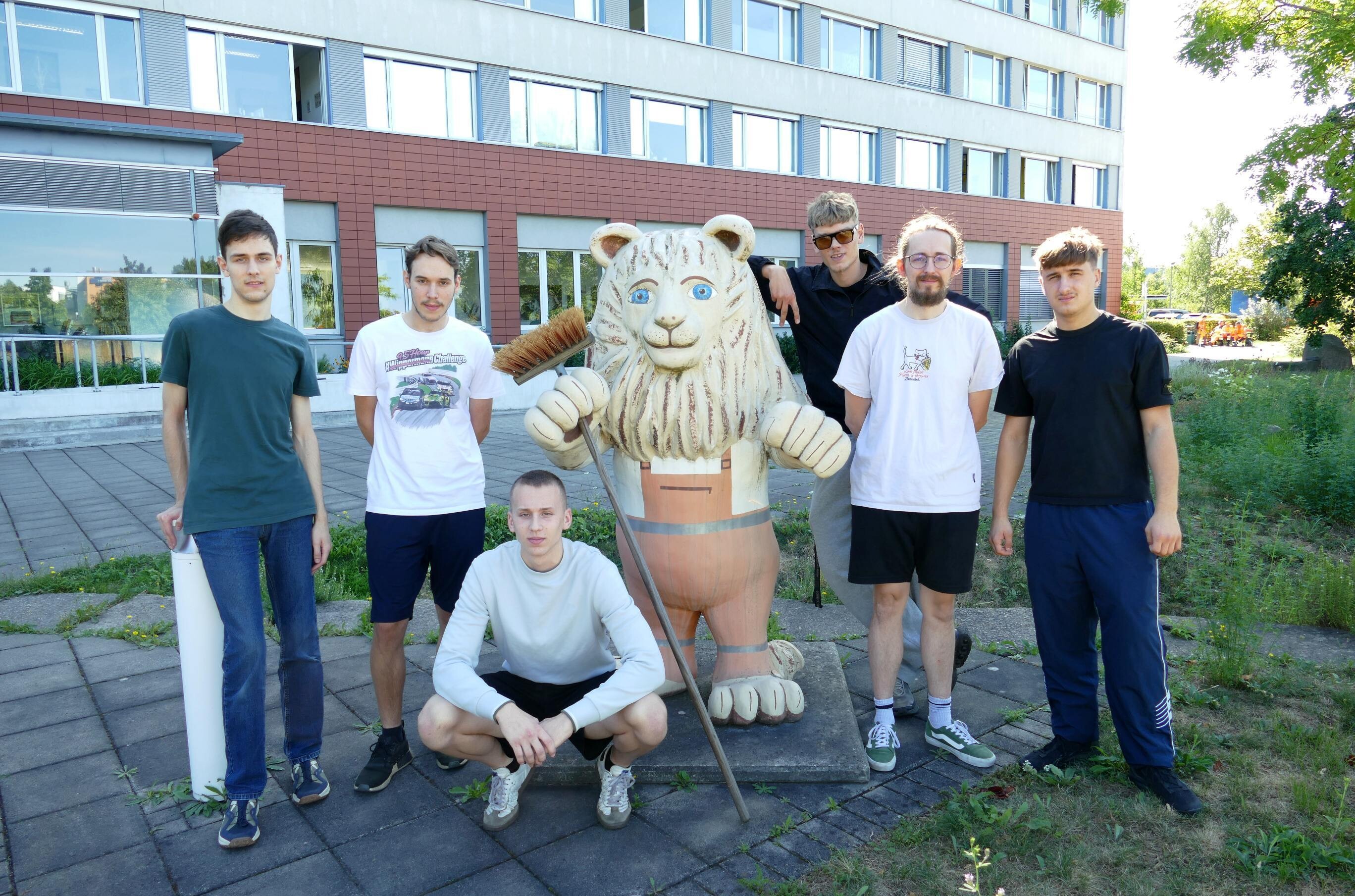 Sechs junge M&auml;nner posieren mit einer L&ouml;wenstatue vor einem Geb&auml;ude der Stadtreinigung Leipzig