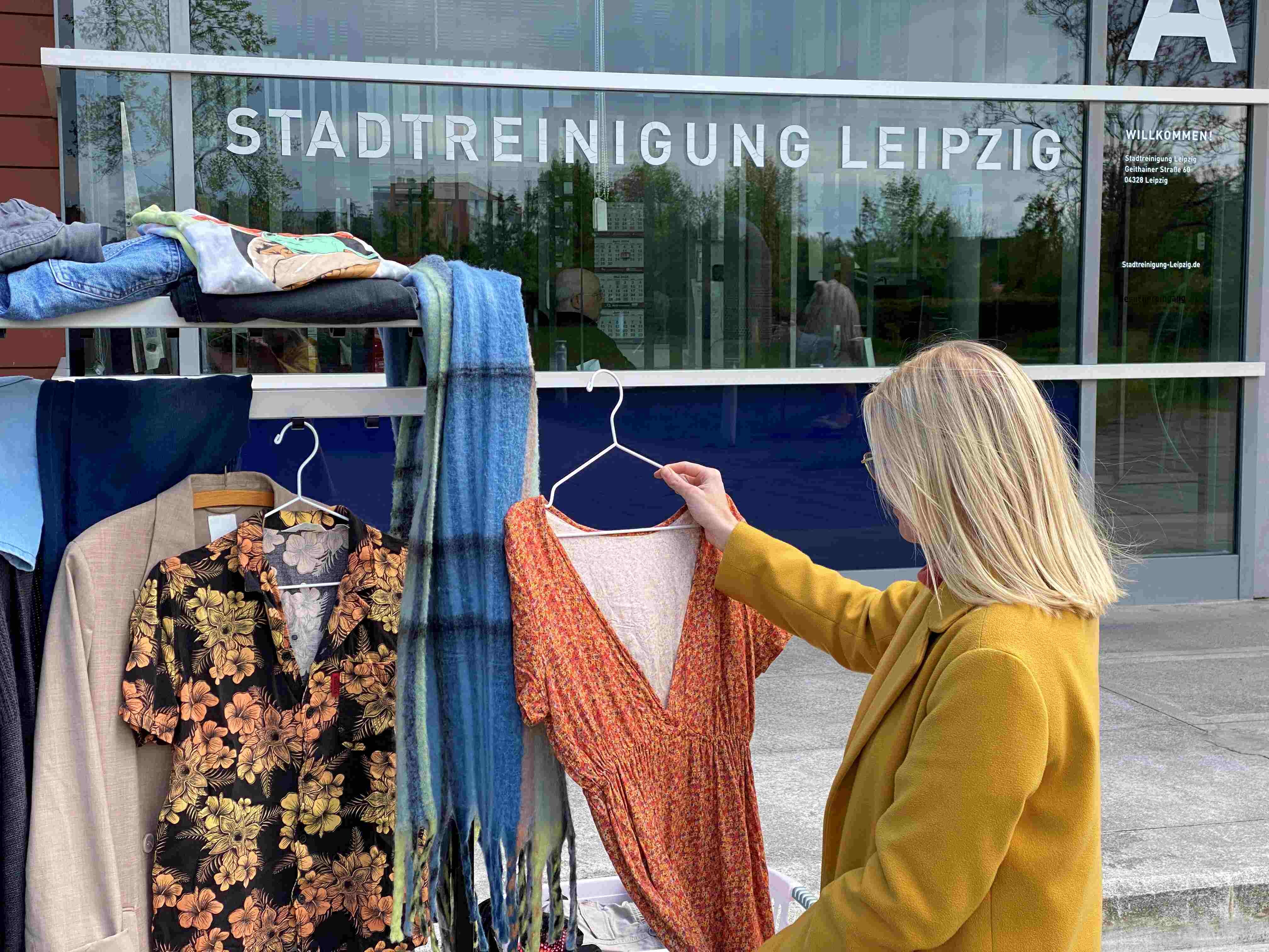 Frau steht vor einem Kleiderständer. Sie hält ein Kleid in den Händen.