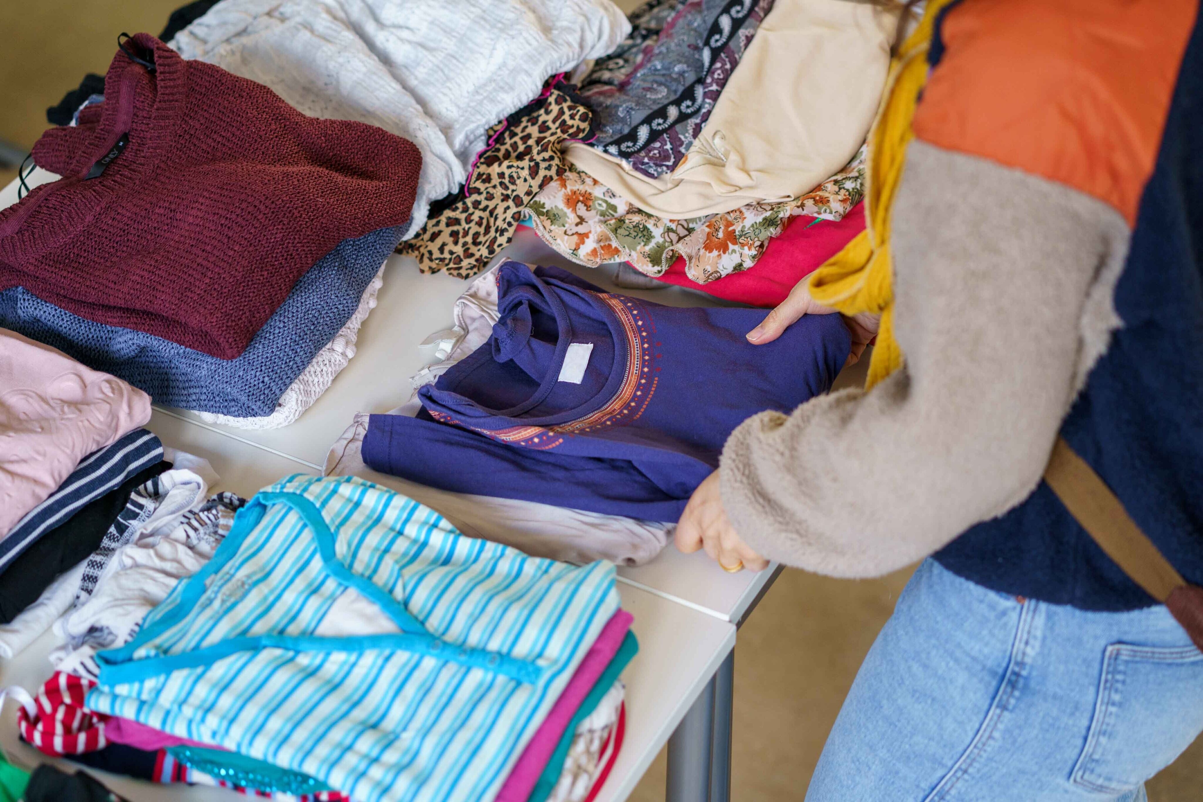 Person steht an einem Tisch auf welchem Kleidungsst&uuml;cke liegen