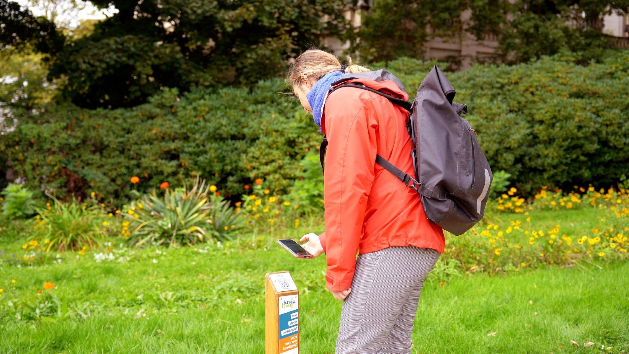 Frau steht im Gr&uuml;nen und scannt einen QR-Code auf einem Holzpanel ab