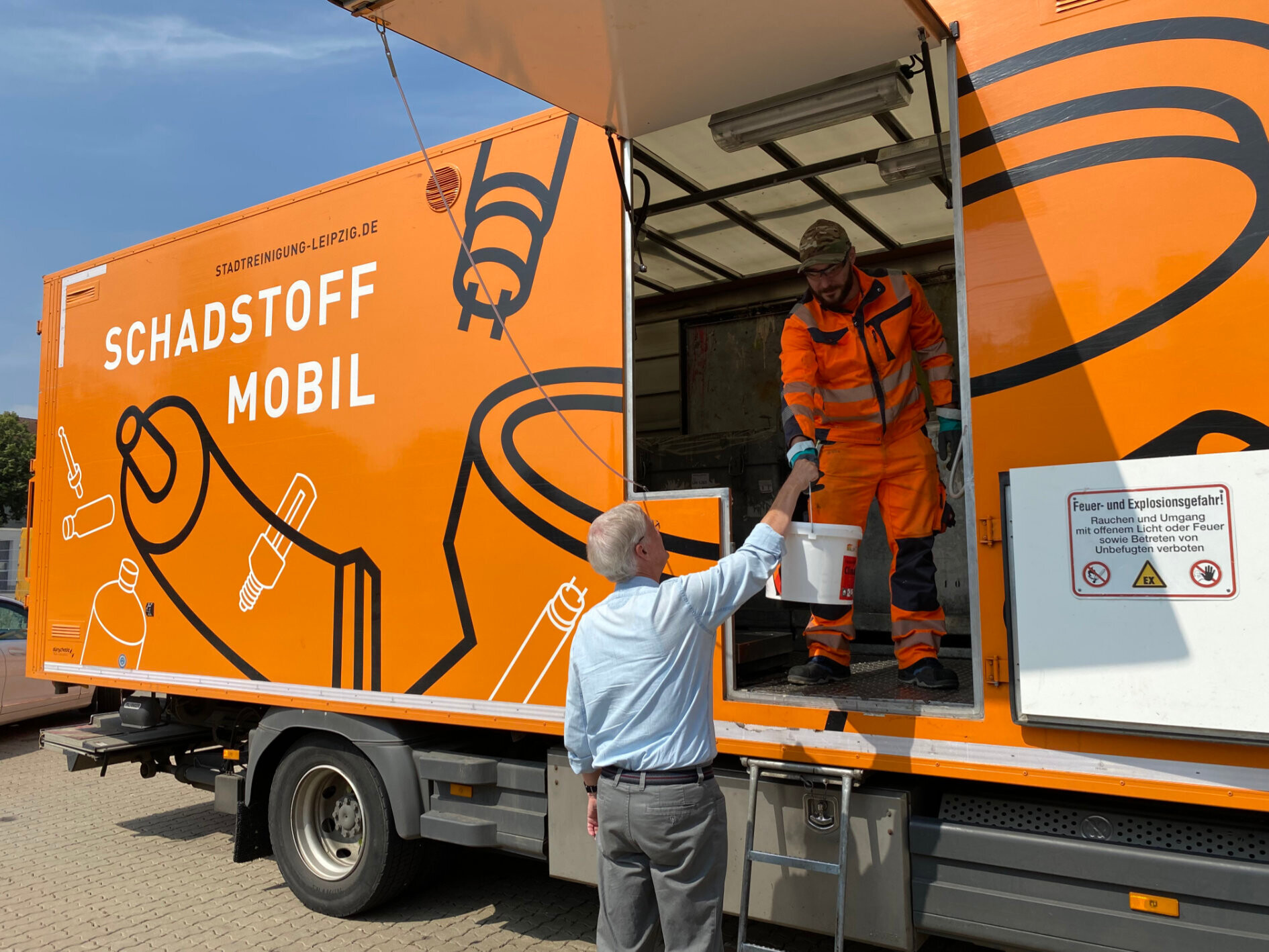 Ein Mitarbeiter im Schadstoffmobil nimmt einen Eimer Farbe von einem Herren entgegen