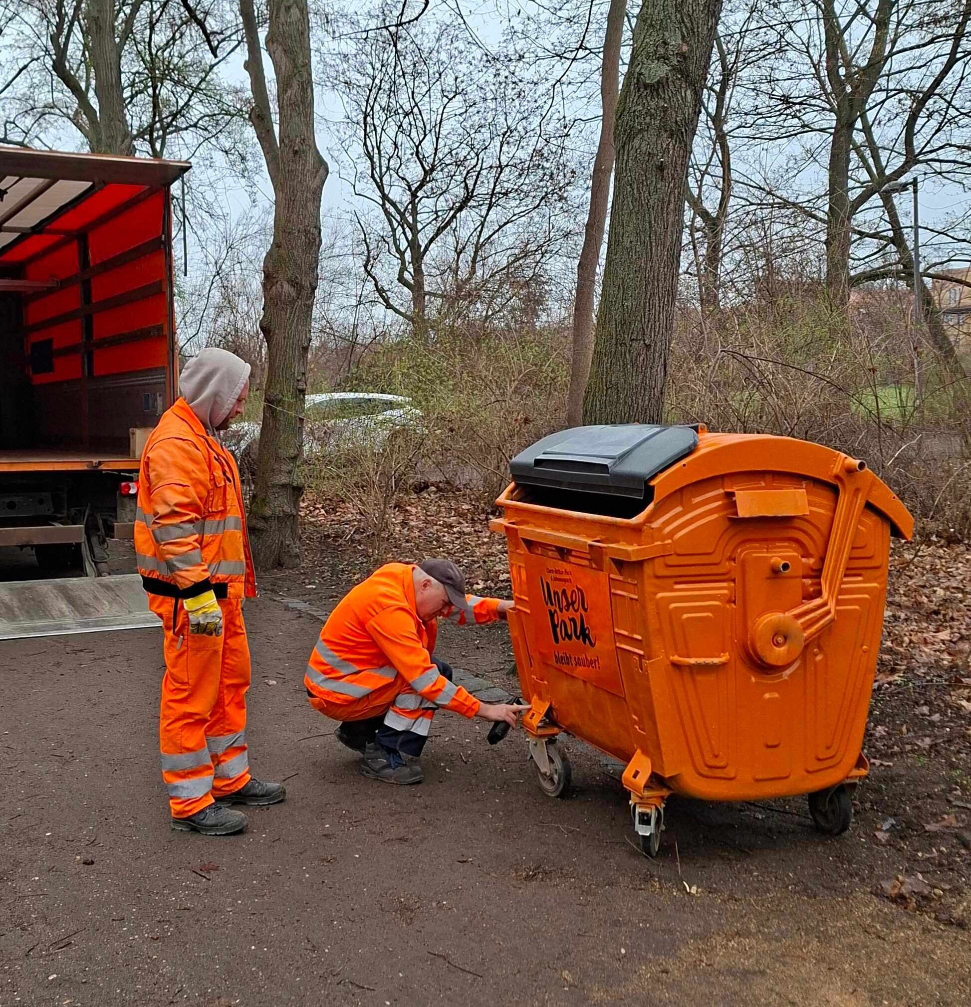 Zwei Mitarbeiter der Stadtreinigung stellen einen Parkcontainer im Mariannenpark auf.
