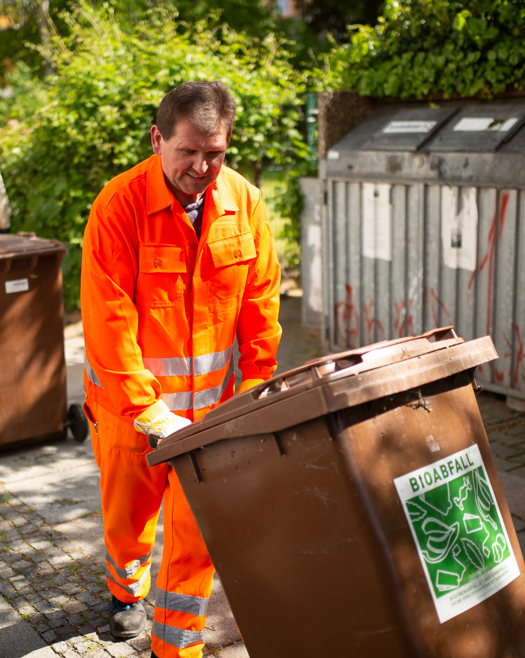 Mitarbeiter zieht braune Biotonne zum Entleeren.