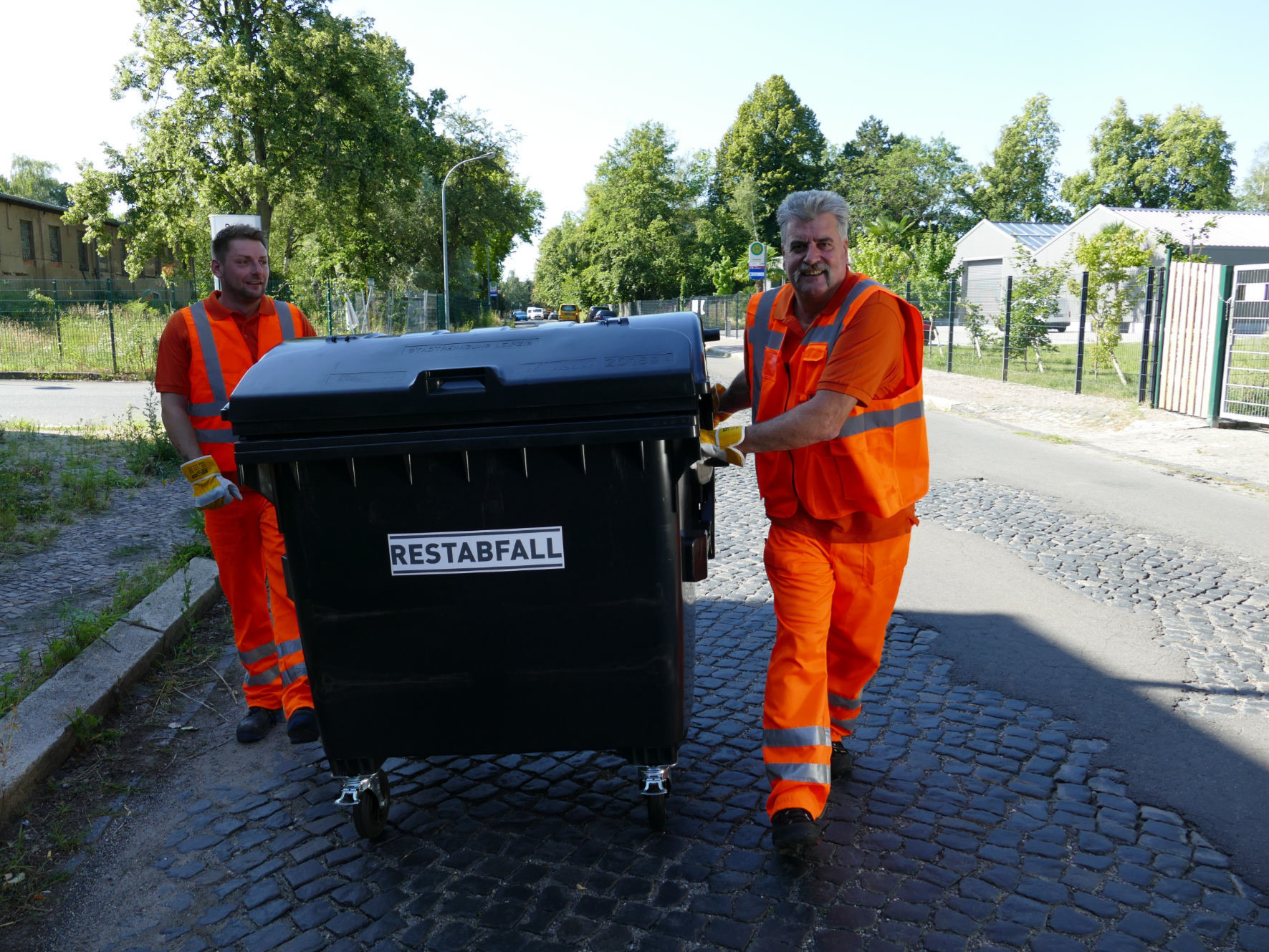 Müllwerker schieben große Abfalltonne
