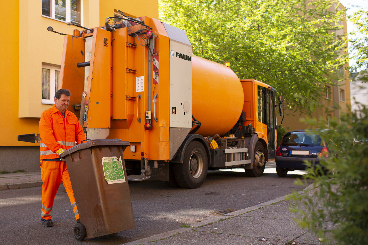 Mitarbeiter der Stadtreinigung zieht Biotonne zum Abfallsammelfahrzeug