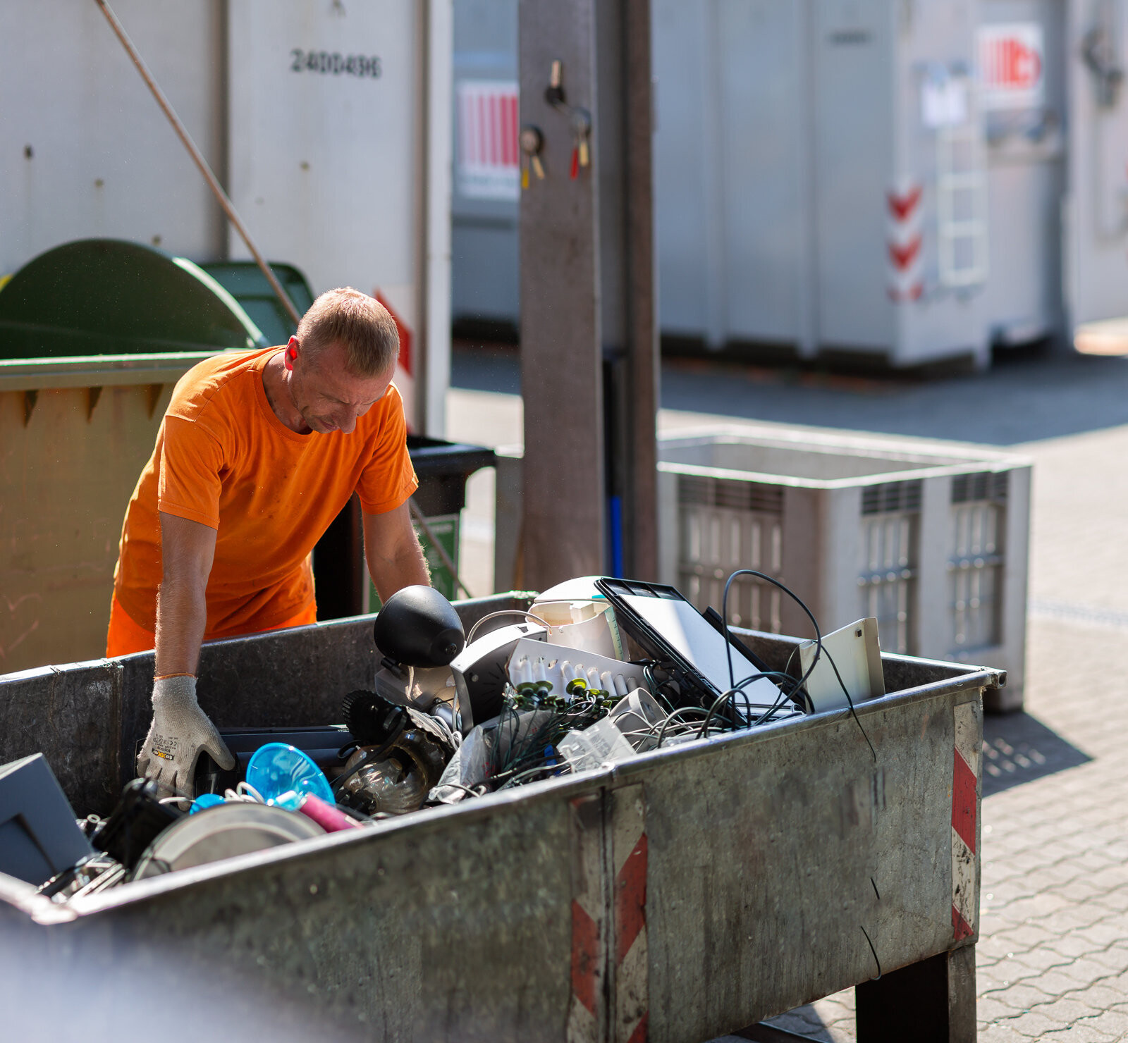 Mitarbeiter der Stadtreinigung steht hinter Container voller Elektroaltgeräte und sortiert diese.