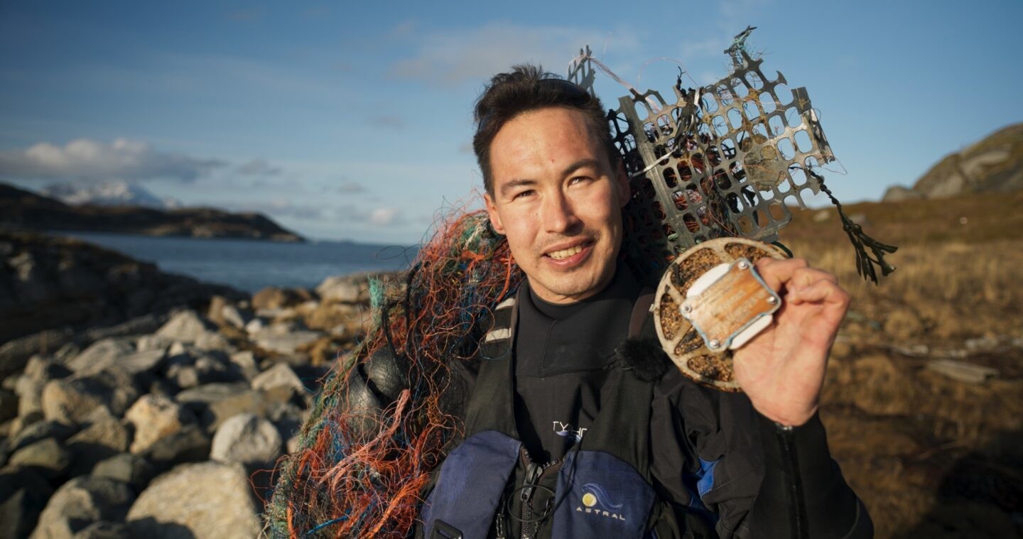 Mann schultert Plastikabfälle vor einem Norwegischen Fjord.