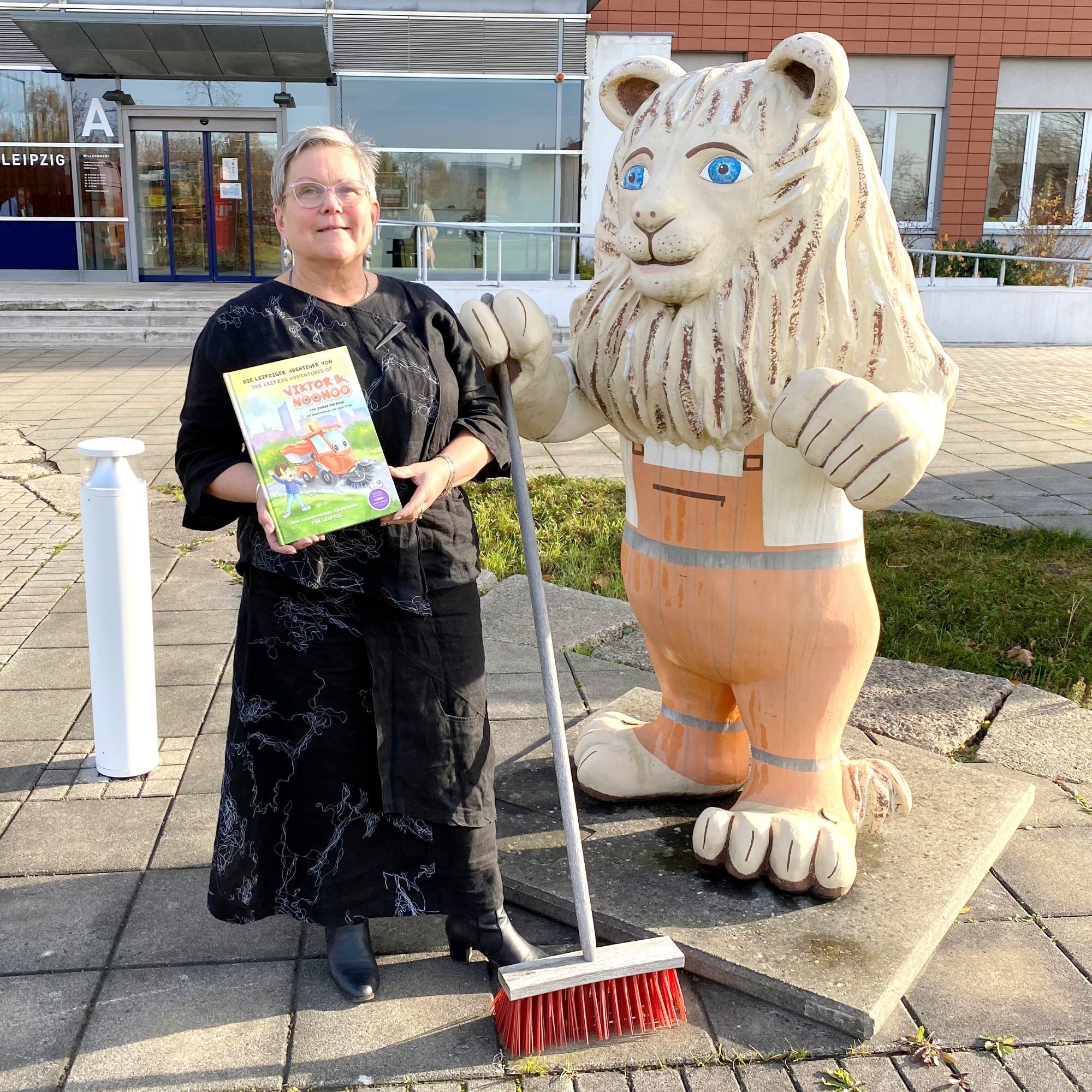 Eine Frau steht mit einem Buch neben einer Löwenfigur vor dem Stadtreinigungsgebäude.