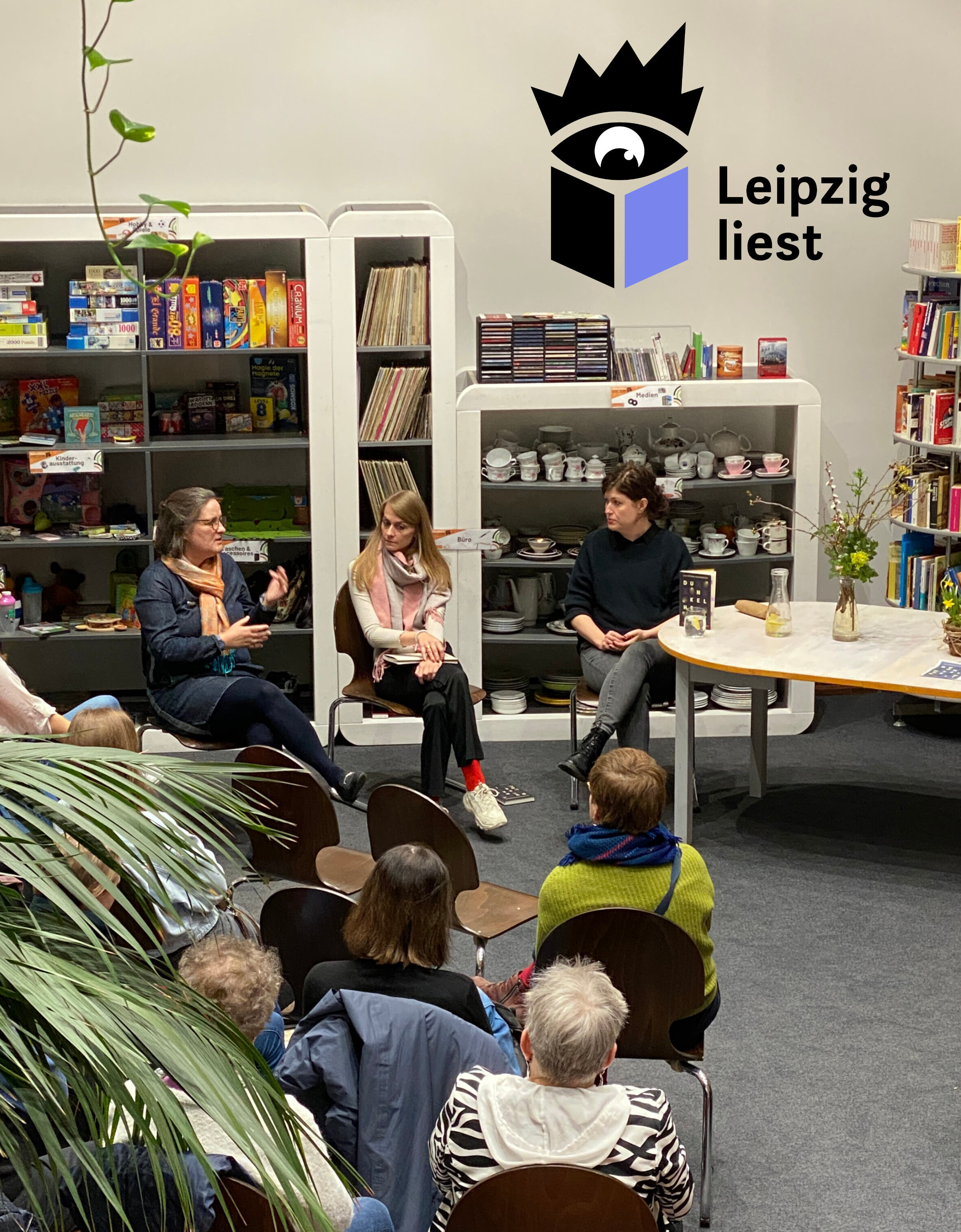 Eine Gruppe von Menschen h&ouml;rt zwei Autorinnen und einer Moderatorin beim Lesen zu