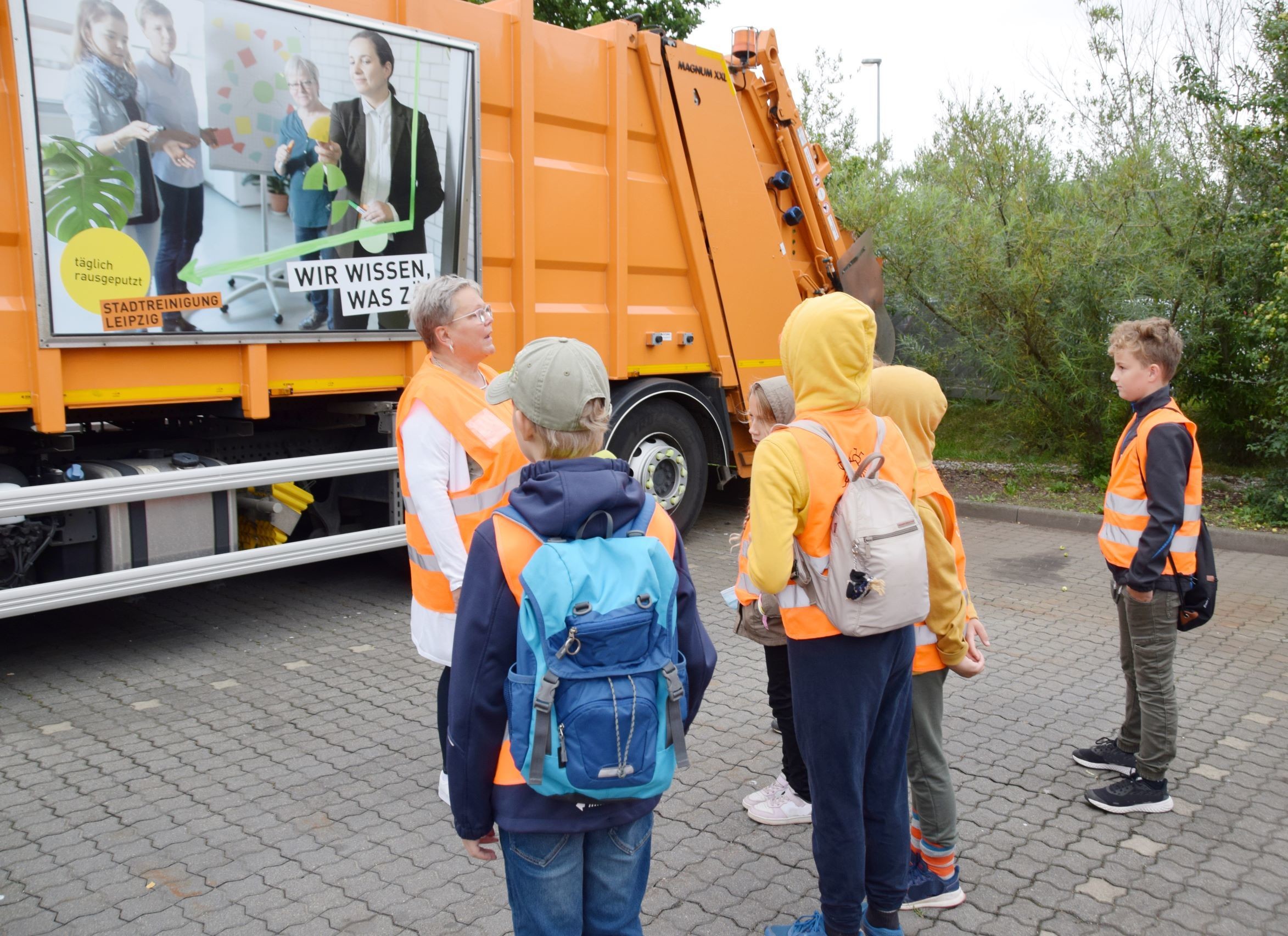 Fünf Kinder stehen mit einer Frau vor einem Abfallfahrzeug.