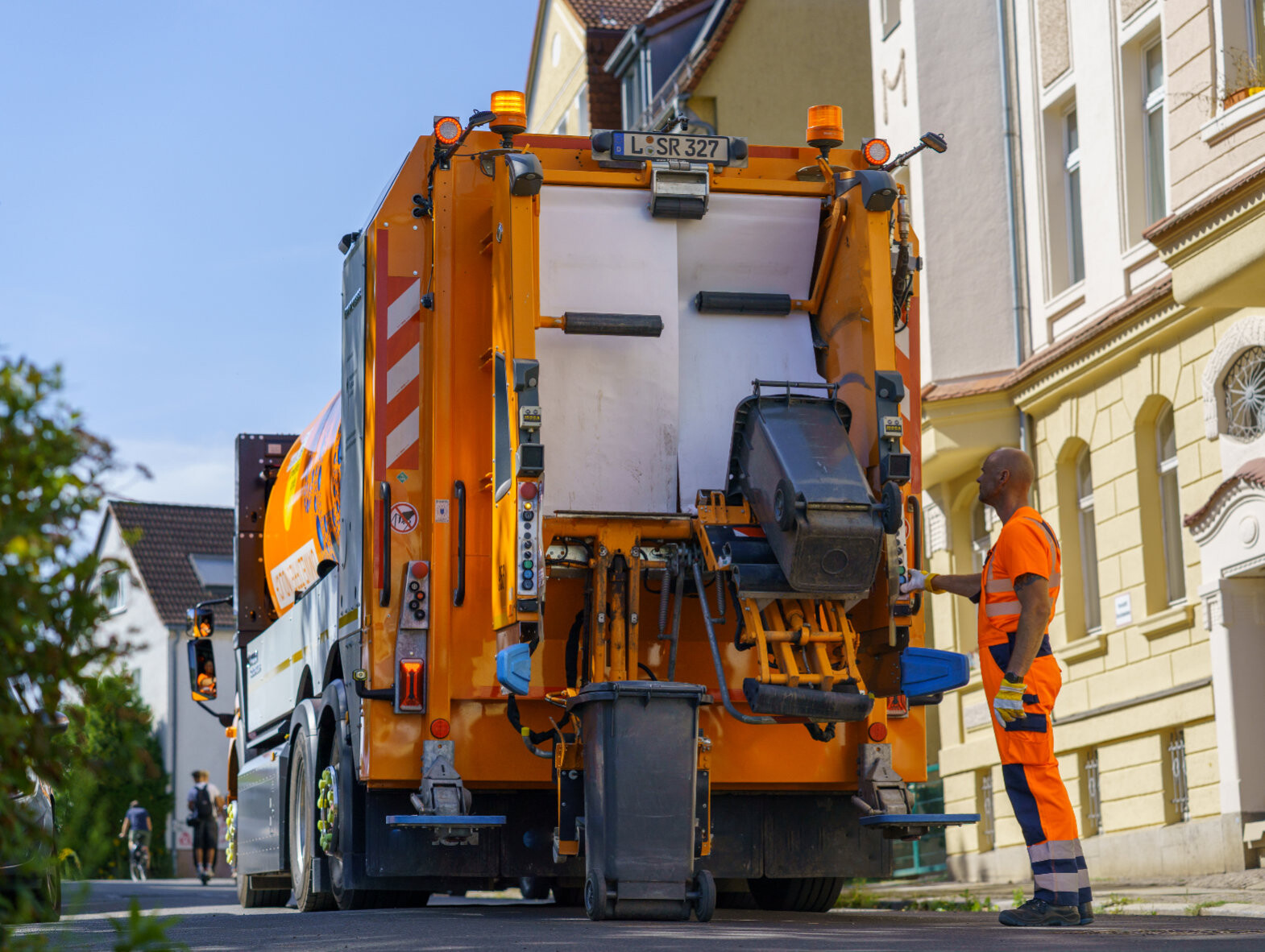Ein M&uuml;llwerker steht hinter einem Abfallsammelfahrzeug und kippt eine kleine Restabfalltonne ab