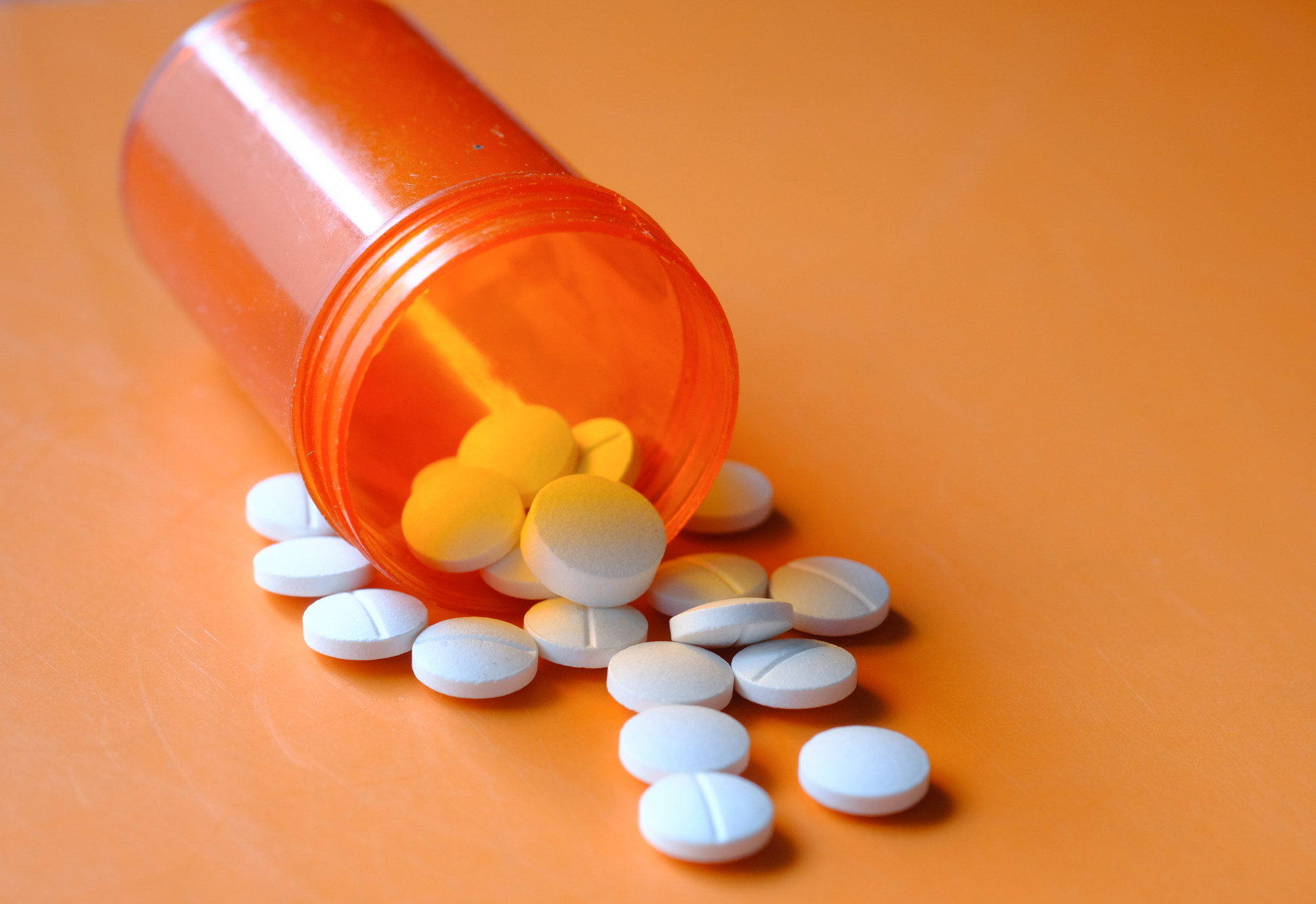 Wei&szlig;e Tabletten fallen aus einer orangenen Dose